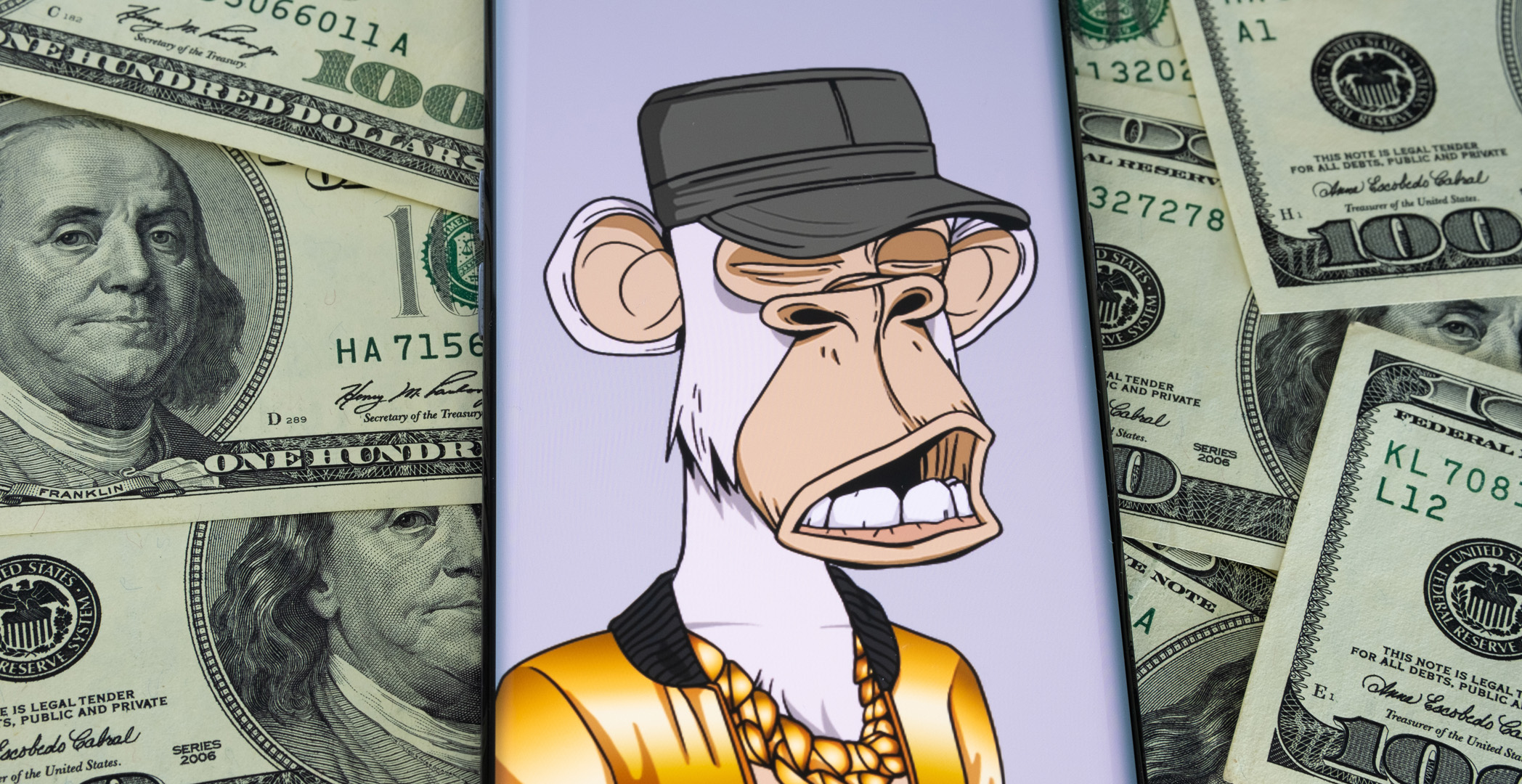 A mobile phone showing a picture of a bored ape NFT, sitting on top of a pile of dollar bills